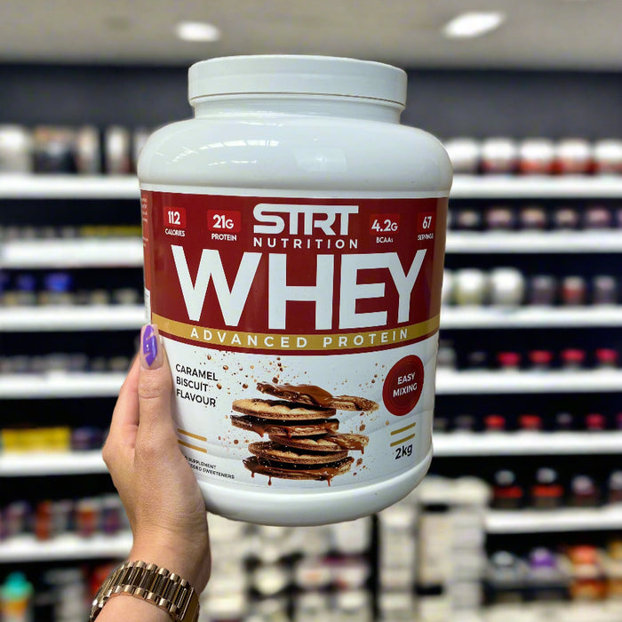 MYSUPPLEMENTSHOP’s Abbie, sporting branded purple nails, holding a tub of whey protein powder in-store, showcasing the nutritional information label with 22g protein per scoop and 67 servings clearly visible.

